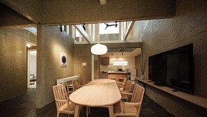 A modern interior with a large dining table surrounded by chairs, a kitchen area, and a large flat-screen TV mounted on the wall. - Furugo BASE (Oita)