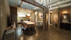 A spacious interior with a high ceiling, a dining area with a large table and chairs, a kitchen with a sink, and a staircase. - Furugo BASE (Oita)