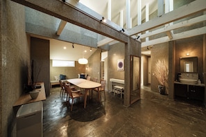 A spacious interior with a high ceiling, a dining area with a large table and chairs, a kitchen with a sink, and a staircase.