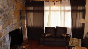 Una sala de estar con pared de piedra, televisor de pantalla plana, sofá negro y mesa de centro de madera.