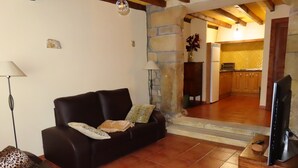 Una sala de estar con sofá, televisión y una cocina al fondo.