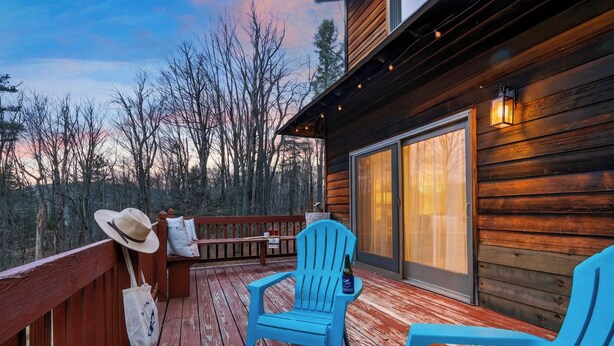 A wooden deck with chairs and a table, a wooden cabin with a glass door, and a forested backdrop. - 6BR + Hot Tub + Firepit + Playroom | Mins to Hunter Mountain + Catskills Hikes (Tannersville)