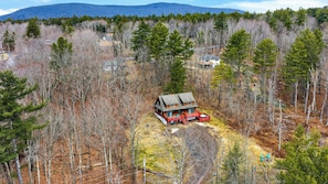 Eine Hütte mit Veranda, umgeben von Wald und Bergen im Hintergrund.