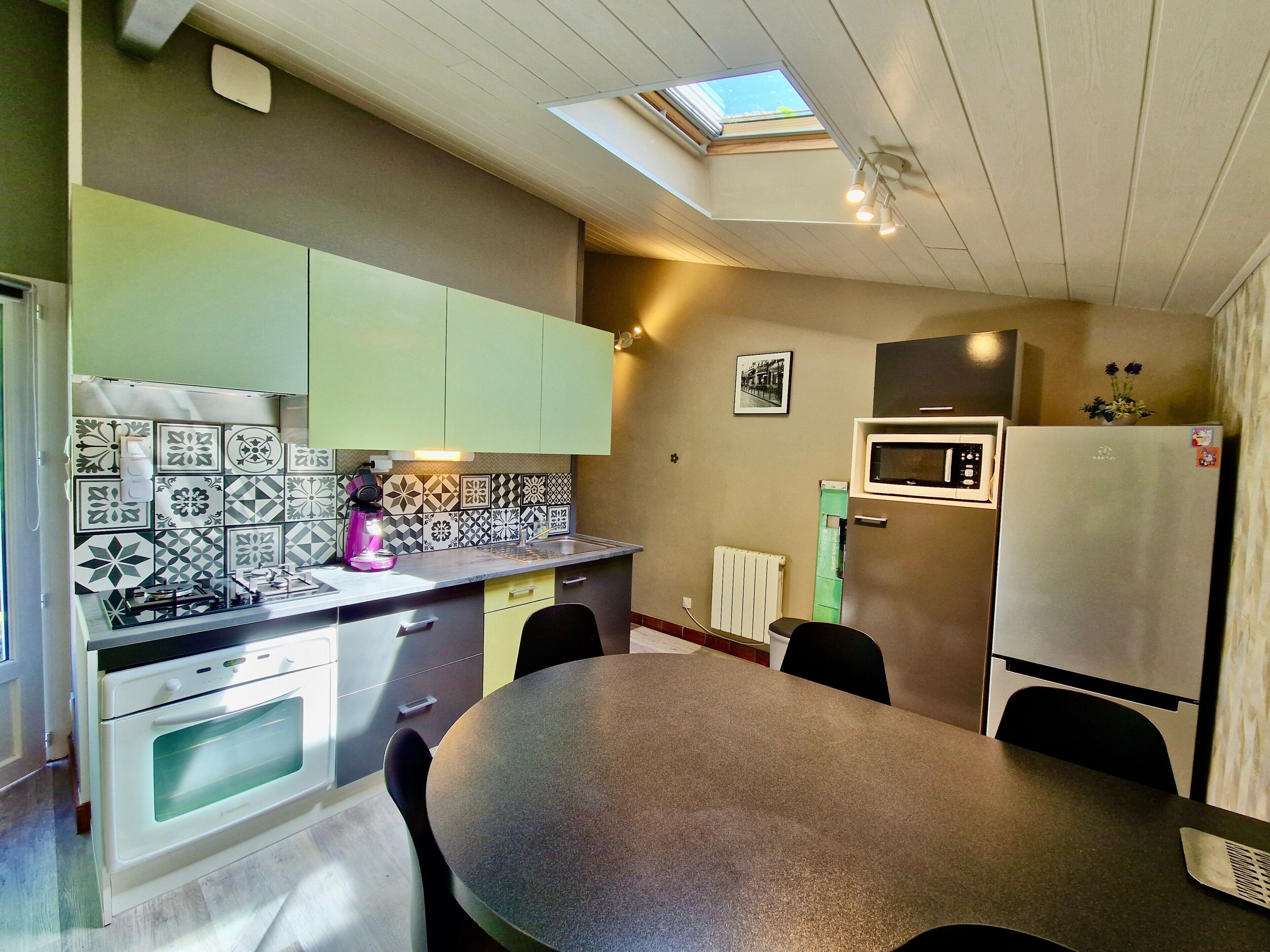 A compact kitchen with a skylight, a microwave, a refrigerator, and a dining table with chairs.