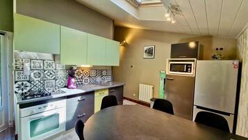 A compact kitchen with a skylight, a microwave, a refrigerator, and a dining table with chairs.