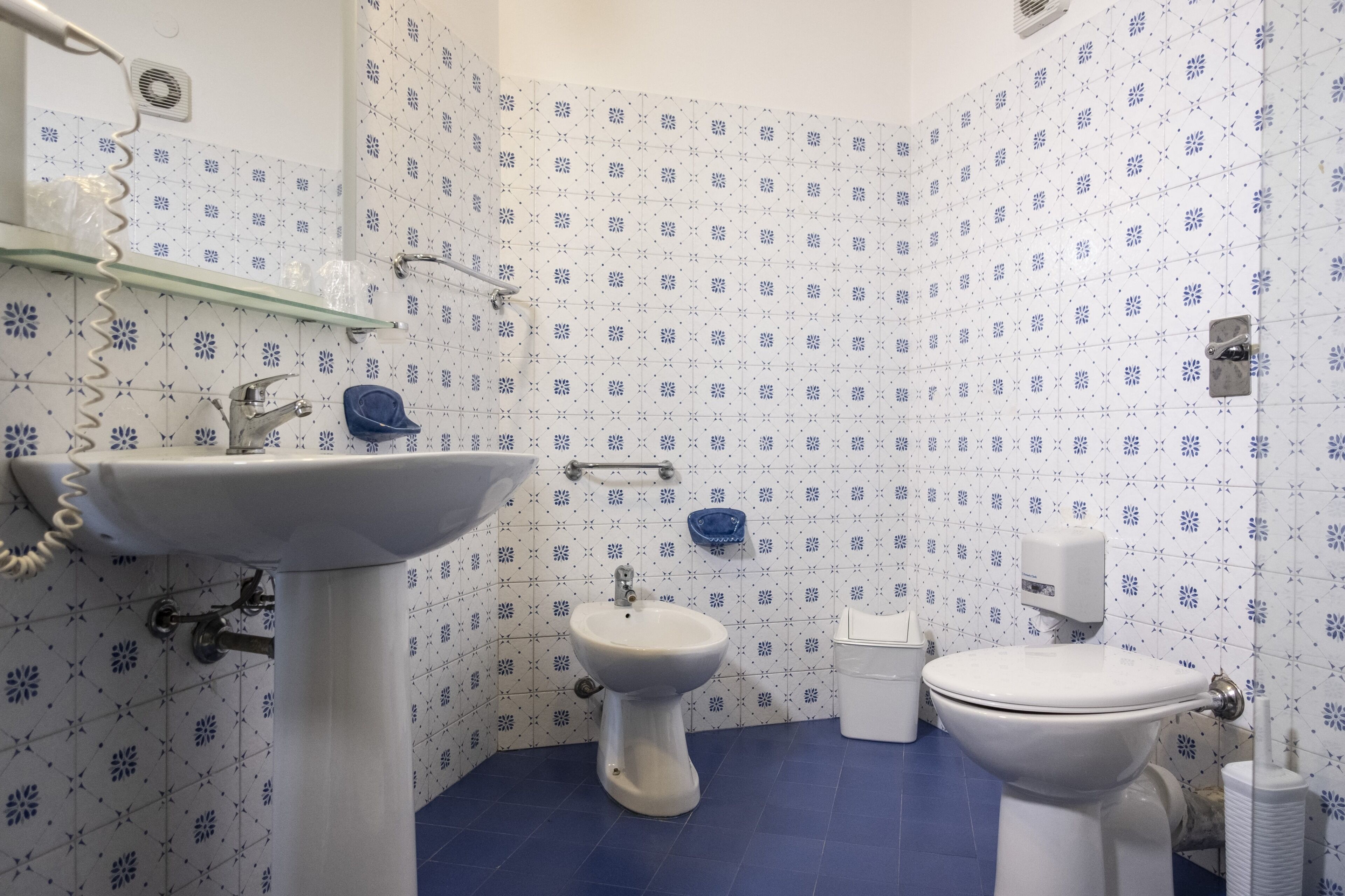 Un baño con lavamanos, bidé e inodoro, con azulejos de patrón azul y blanco.