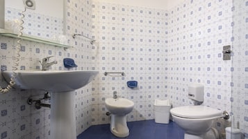 Un baño con lavamanos, bidé e inodoro, con azulejos de patrón azul y blanco.