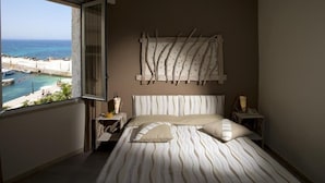 A bedroom with a bed, a nightstand, a lamp, a view of the beach, and a wall art piece. - Hotel Tirreno (Pizzolungo)