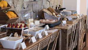 A buffet with various food items, including fruits, cheeses, and meats, set against a stone wall backdrop. - Hotel Tirreno (Pizzolungo)