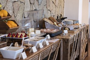 En buffé med ett varierat utbud av mat, inklusive frukt, ostar och kött, placerad framför en bakgrund av en stenmur.