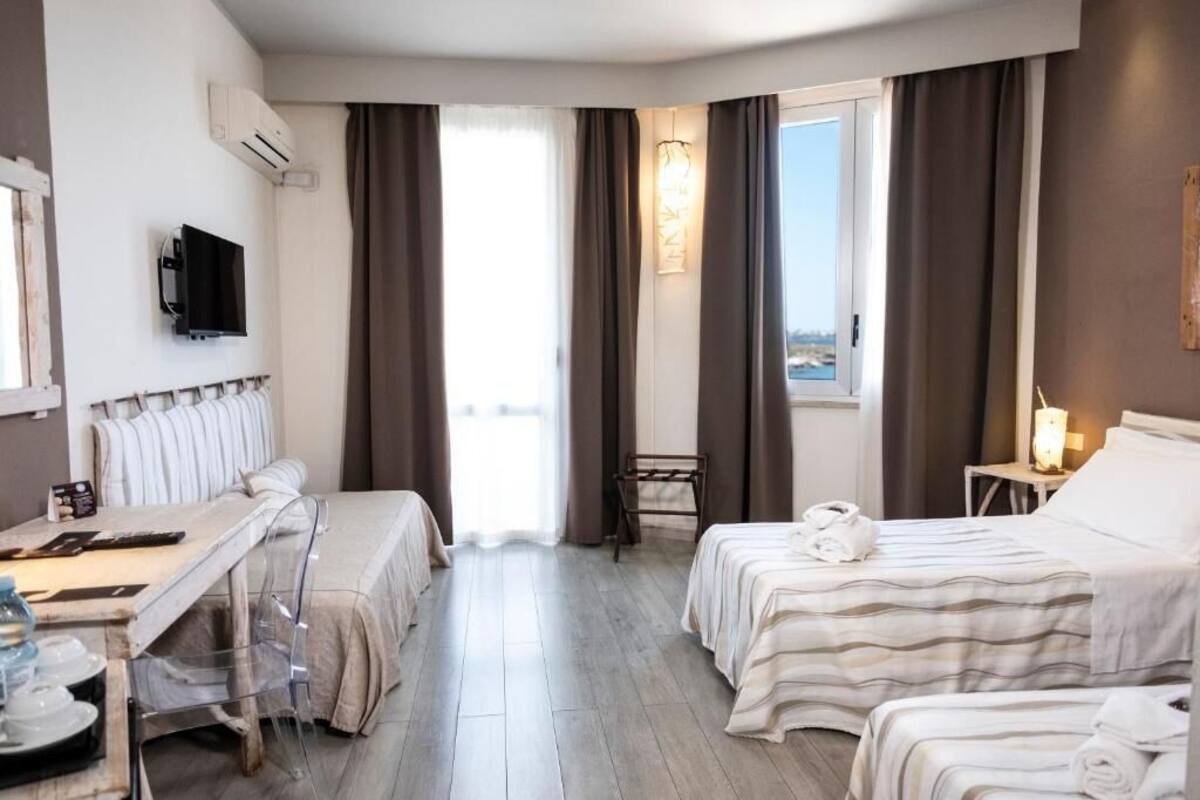 Habitació d'hotel amb dos llits, una taula de treball, una cadira, un televisor i una finestra amb cortines.