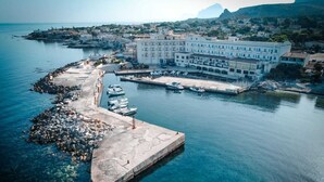An aerial view of a coastal town with a marina, a large hotel with multiple floors, and rocky terrain. - Hotel Tirreno (Pizzolungo)