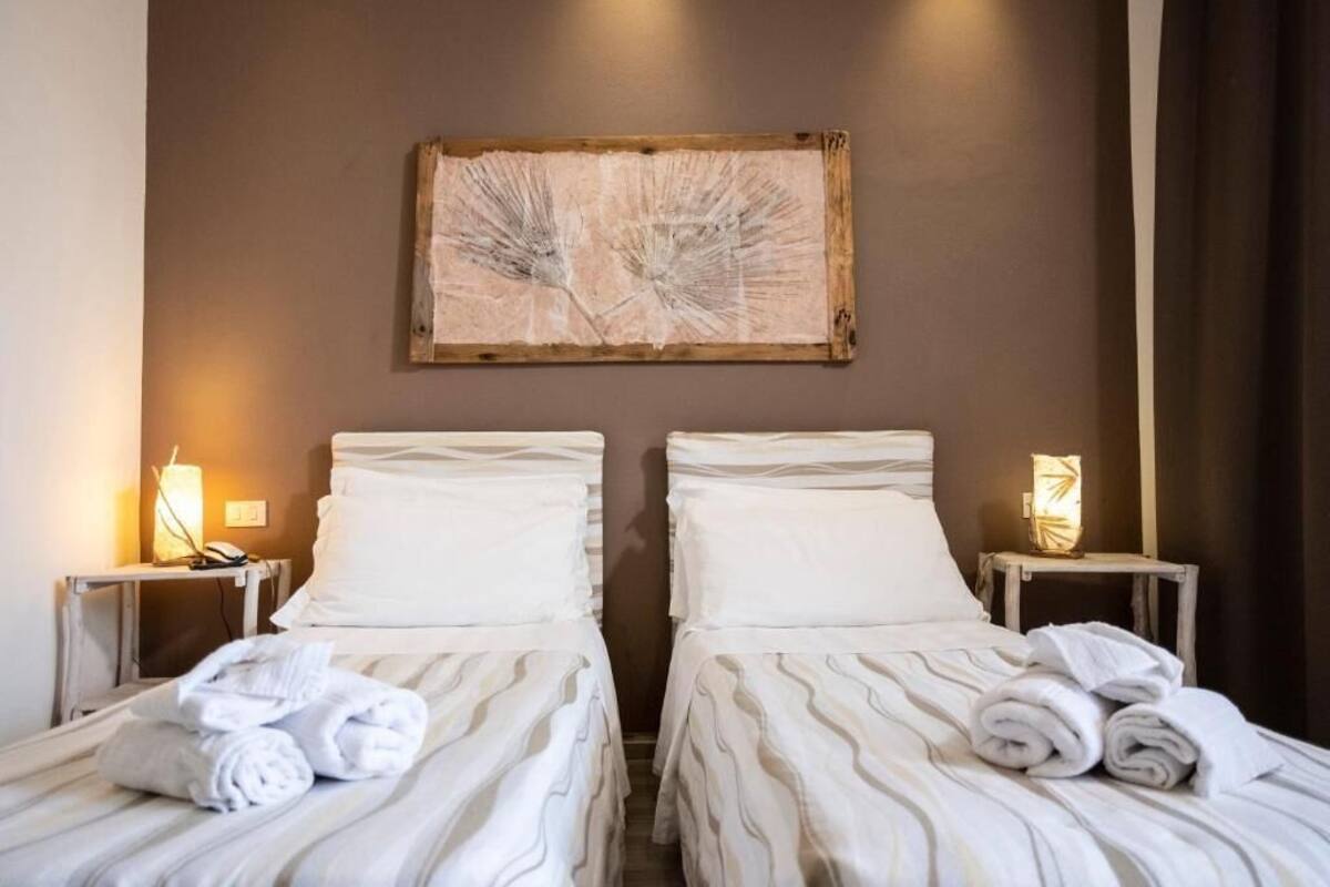 Una habitació d'hotel amb dos llits, cadascun amb un llençol i coixins amb estria blanca, un panell de capçal de fusta i una obra d'art penjada a la paret.