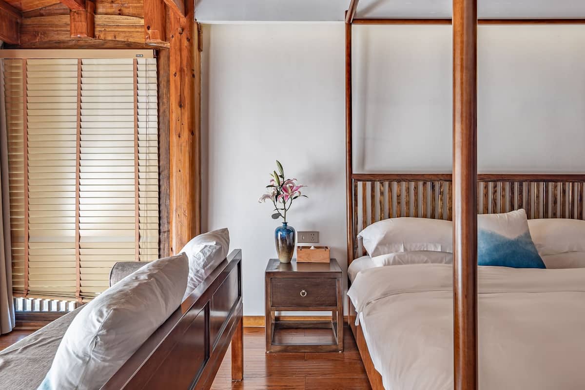 Een slaapkamer in chaletstijl met een hemelbed, een houten bankje en een nachtkastje met een vaas.