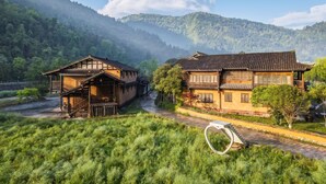 Traditional buildings with wooden structures and tiled roofs, surrounded by lush greenery and hills. - L Resident Dragon Cave Resort - Zhangjiajie (Zhangjiajie)