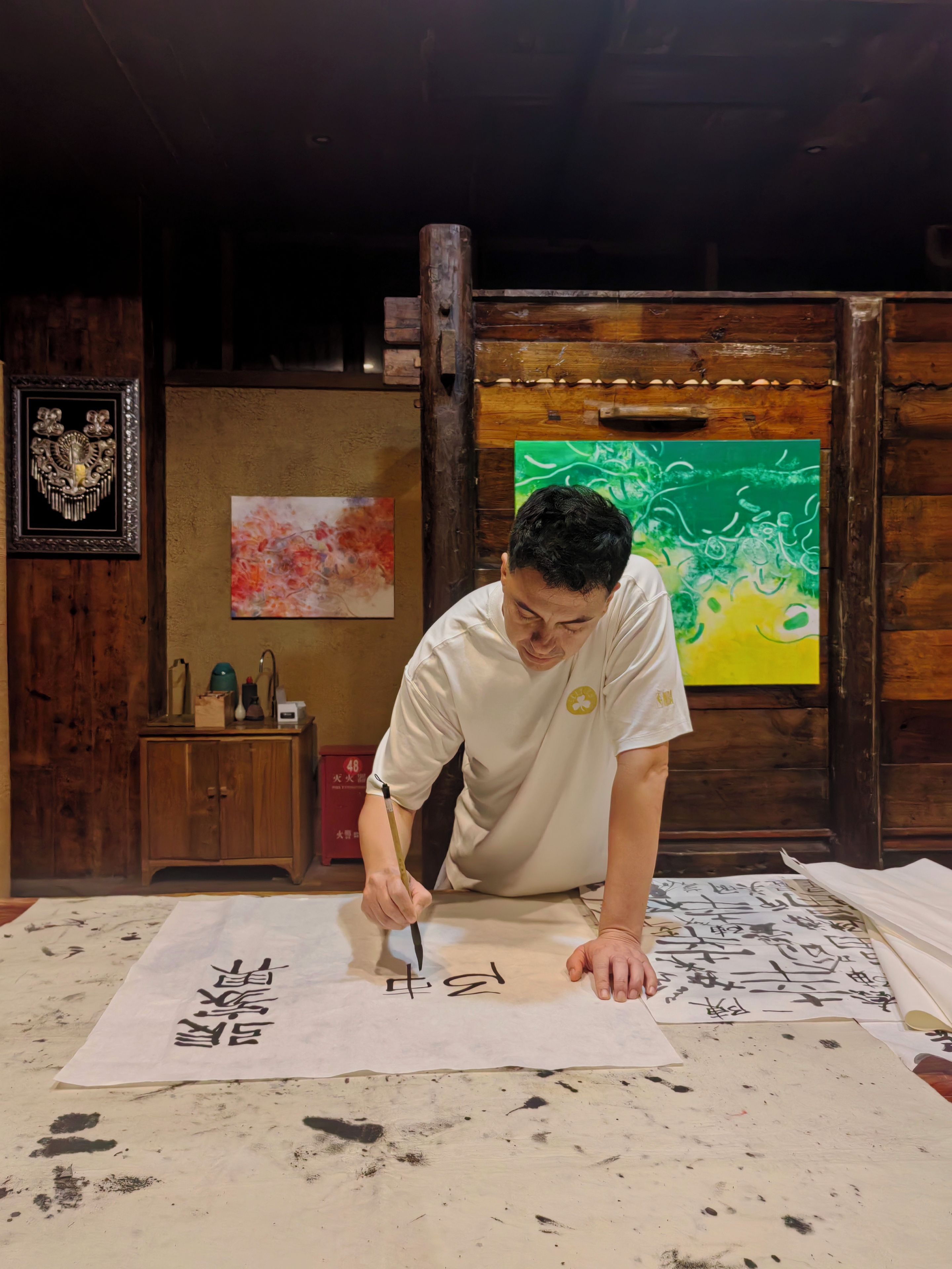 A person writing on a large paper with calligraphy tools.