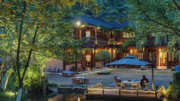 A traditional wooden building with a courtyard, outdoor seating, and a small water feature. - L Resident Dragon Cave Resort - Zhangjiajie (Zhangjiajie)