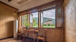 A room with a wooden desk, two chairs, a window with wooden shutters, and a view of traditional thatched-roof buildings. - L Resident Dragon Cave Resort - Zhangjiajie (Zhangjiajie)