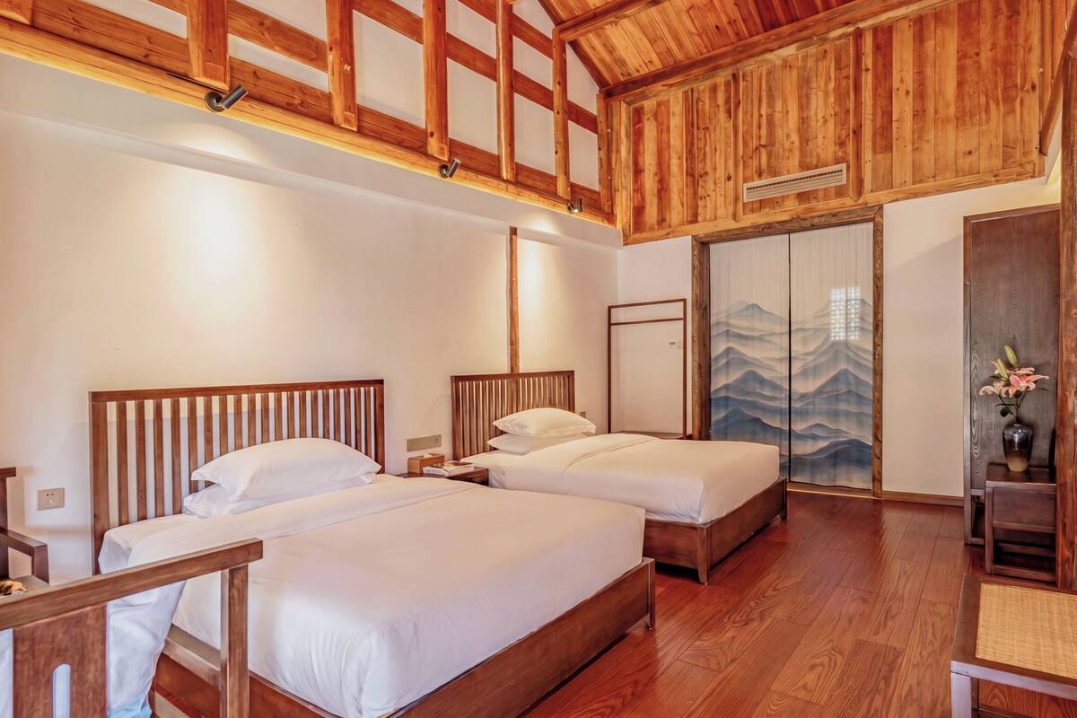 Een hotelkamer met twee bedden, houten balken in het plafond, een traditionele schuifdeur en een klein tafeltje met een bloevas.