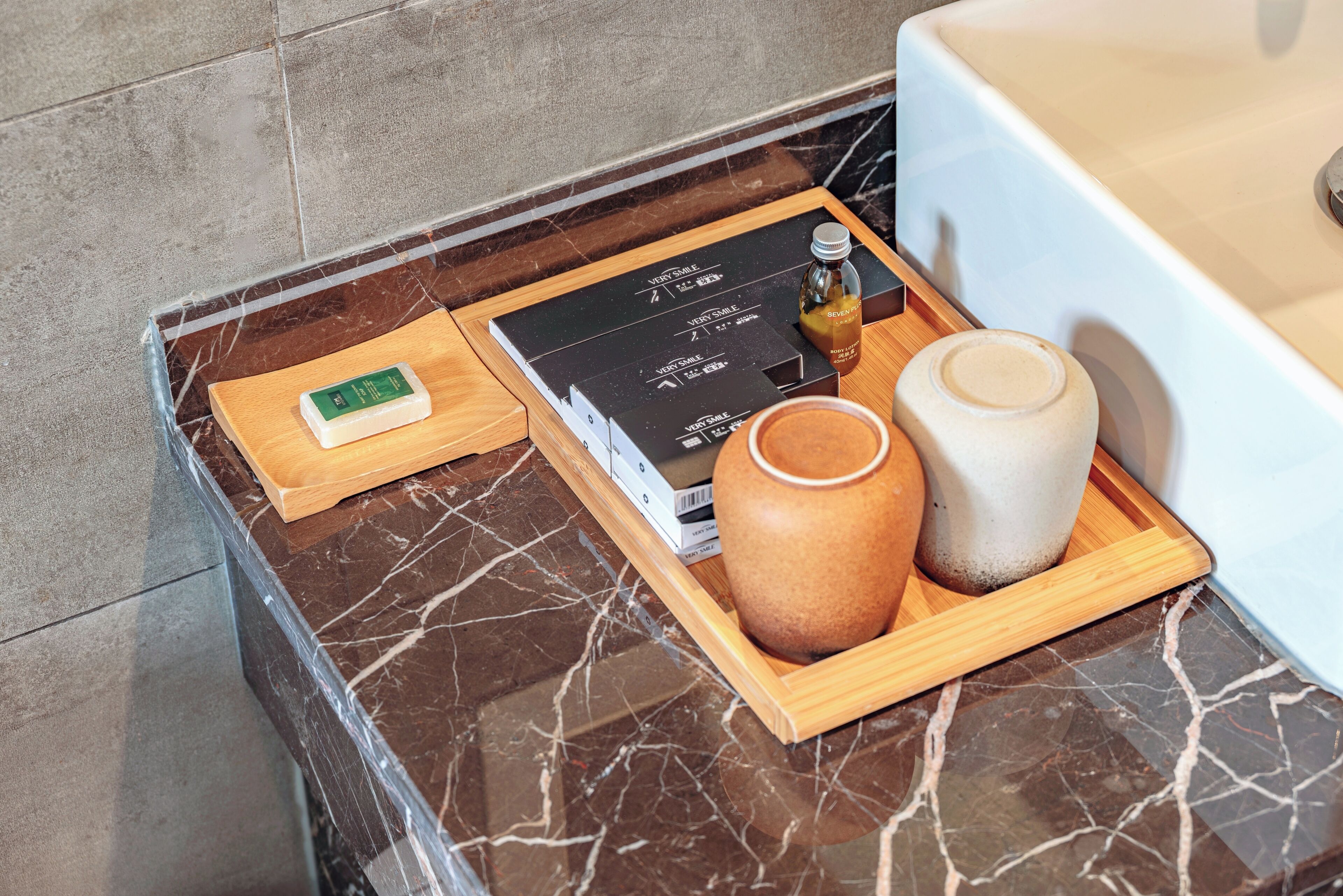 Une salle de bain avec un comptoir en marbre, un plateau en bois sur lequel se trouvent une bouteille, un savon et un vase.