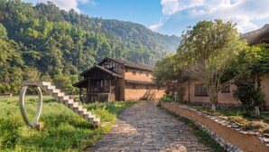 A traditional building with a stone staircase leading to a wooden structure, surrounded by lush greenery and mountains. - L Resident Dragon Cave Resort - Zhangjiajie (Zhangjiajie)