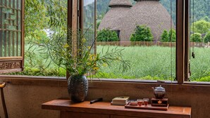 A window with a view of traditional thatched-roof buildings, a wooden desk with a vase of flowers, and a tea set. - L Resident Dragon Cave Resort - Zhangjiajie (Zhangjiajie)
