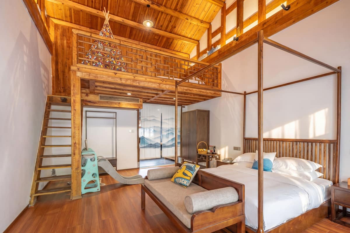 Een ruime slaapkamer met een hemelbed, een houten trap en uitzicht op het groen.