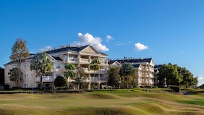 A large, multi-story hotel with balconies, a golf course in the foreground, and a clear blue sky. - Family 3BR Retreat – Water Park, Pools & Disney Access (Kissimmee)