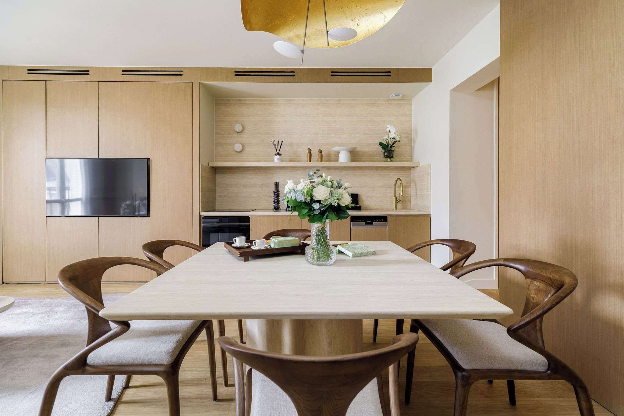 A modern dining area with a wooden table, chairs, and a TV mounted on the wall.