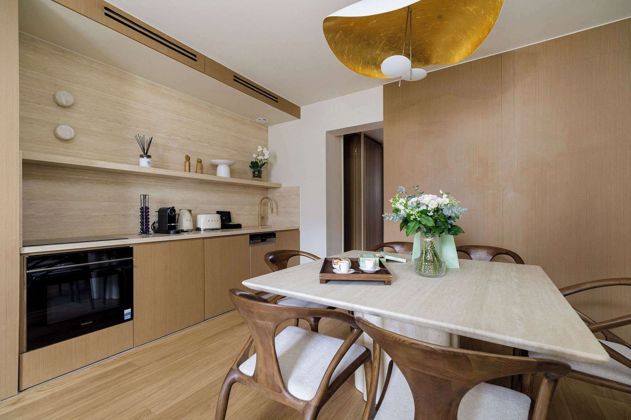 A modern kitchen with wooden cabinets, a built-in oven, and a dining area with a table and chairs.