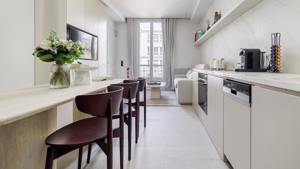 Een moderne keuken met een eethoek, witte kasten en een raam met gordijnen.