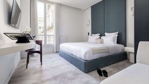 Een moderne hotelkamer met een bed, een bureau, een stoel en een groot raam.