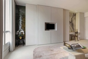 A modern living room with a flat-screen TV mounted on a wall, a small table with a book, and a decorative plant. - A Splendid 2-BR/2Ba w/ Services - Champs Elysées (Paris)