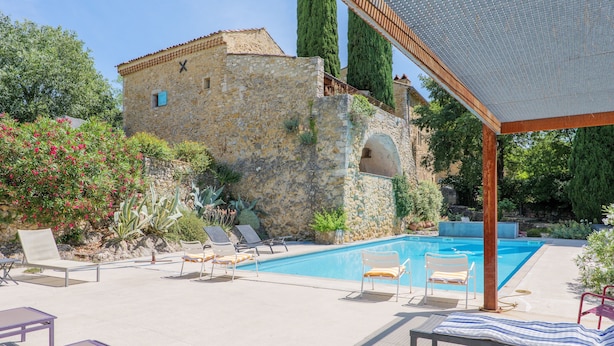 A stone building with a pool, lounge chairs, and a pergola.