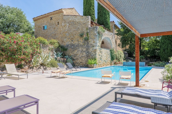 A stone building with a pool, lounge chairs, and a pergola.