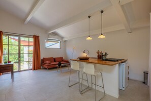 Een moderne keuken met een bar, een eettafel met stoelen, en een bank in een lichte woonkamer met grote ramen.