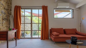 A room with a stone wall, a wooden table with bowls, a sofa, and a window with curtains.