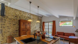 A kitchen with a stone wall, wooden cabinets, a sink, and a dining area with a sofa and table.
