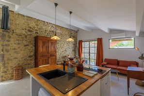 A kitchen with a stone wall, wooden cabinets, a sink, and a dining area with a sofa and table.