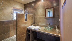 Un baño moderno con un lavabo de vidrio, zona de ducha y un espejo en la pared.