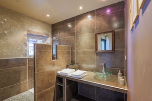 Een moderne badkamer met een glazen wastafel, een douchegedeelte en een spiegel aan de muur.