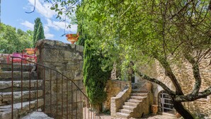Una escalera de piedra conduce a un edificio con barandilla metálica, rodeado de follaje y un cielo despejado.