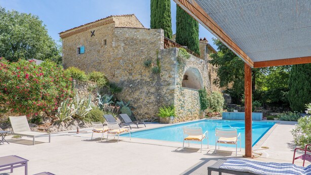 Un edificio de piedra con piscina, sillones de descanso y una pérgola.