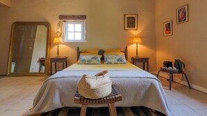 Un dormitorio con cama, dos lámparas de noche, un espejo, una ventana y una silla con un bolso tejido.