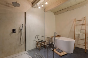 Ein modernes Badezimmer mit Duschkabine aus Glas, freistehender Badewanne und einer Holzleiter.