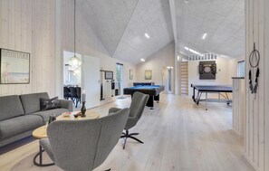 Ein geräumiger Raum mit Poolbillard, Billardtisch und Dartscheibe. Es gibt ein Sofa und einen Esstisch mit Stühlen. Die Wände sind aus Holz und die Decke ist hoch.