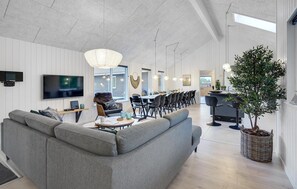 Ein modernes Wohnzimmer mit grauem Sofa, Fernseher und Essbereich mit Stühlen und Tisch.