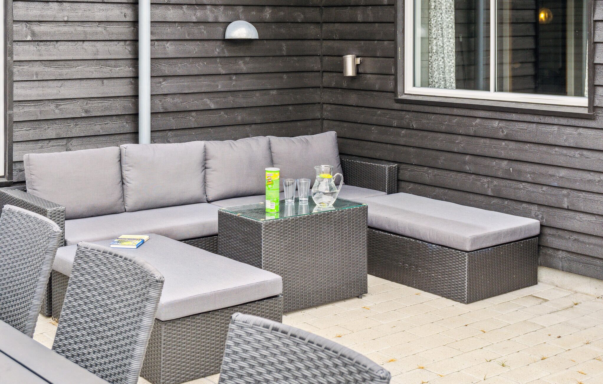 A corner outdoor seating area with a grey sofa, two side tables, and wicker chairs.