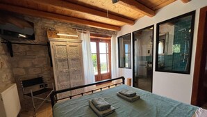 A bedroom with a bed, a wooden ceiling, a stone wall, a window, and a radiator. - Villa Ionis Holiday Villa (Volimes)