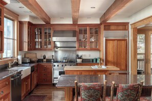 A kitchen with wooden cabinets, a central island, and a dining area with patterned chairs. - Luxury Telluride Mountain Village Home | Hot Tub, Fireplace, Sleeps 12 (Telluride)